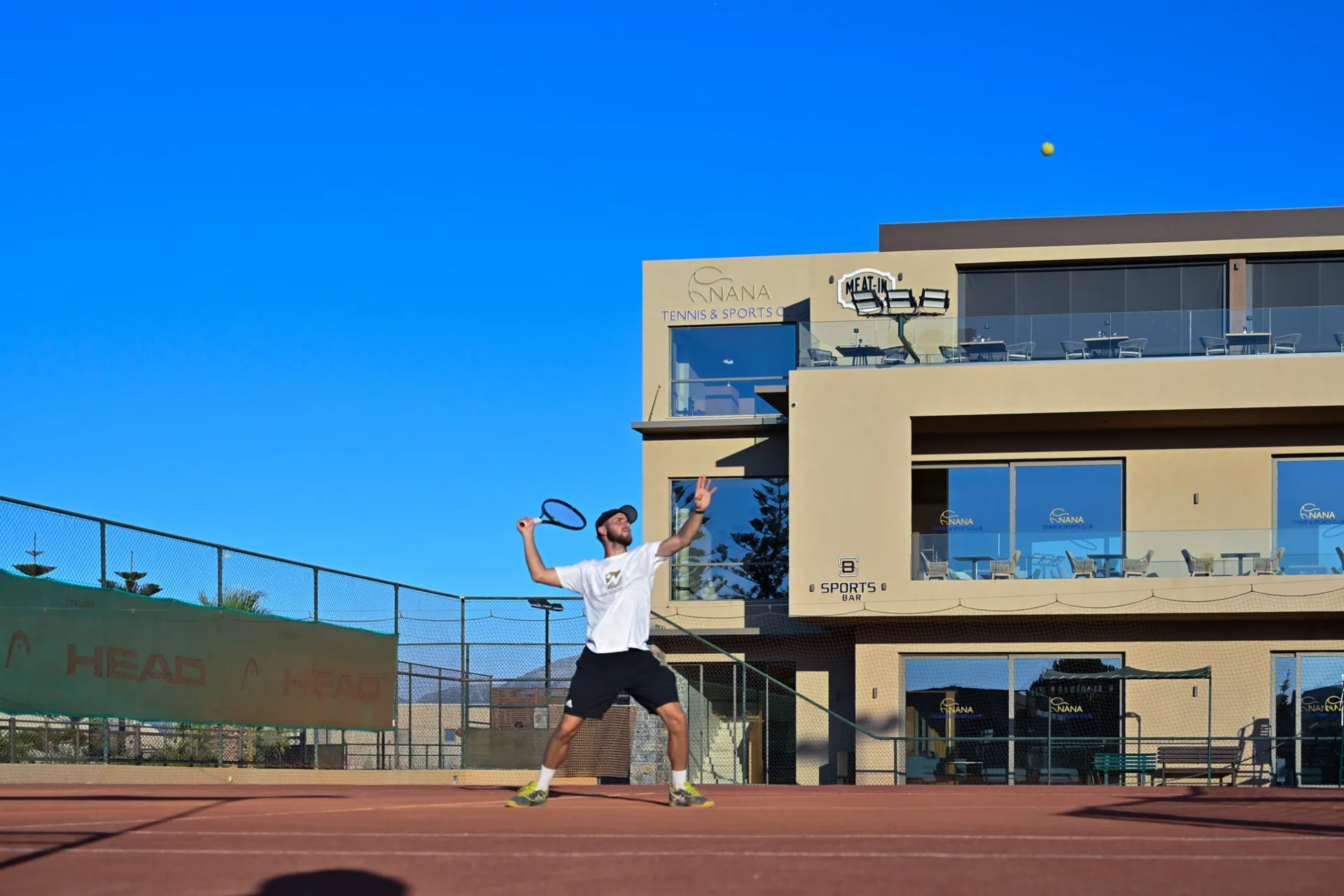 Player serving on a clay court in front of the sports bar
